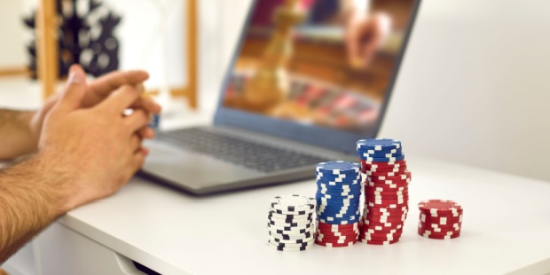 A man entering an online casino on his laptop, with a pile of poker chips at his side. 