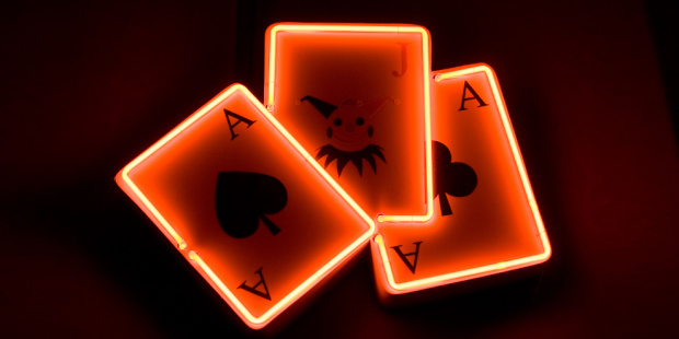 Three playing cards surrounded by orange neon lights.