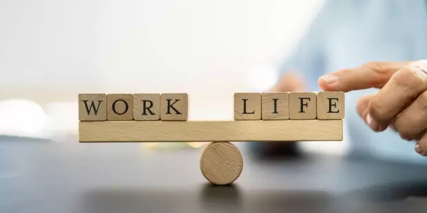 The words 'work' and 'life' are balanced on a wooden plank.