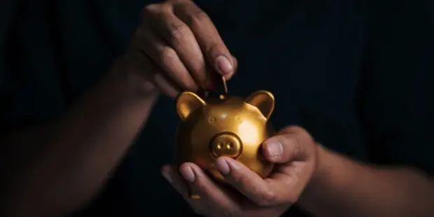 A man putting a coin in a golden piggy bank. 