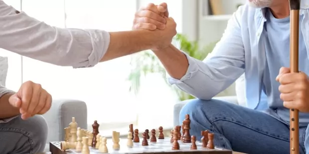 A young man shaking hands with an older gentleman over a chessboard.