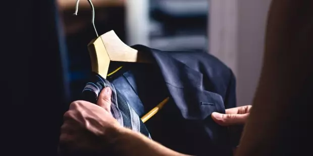 A man holding a suit jacket and tie before getting dressed. 