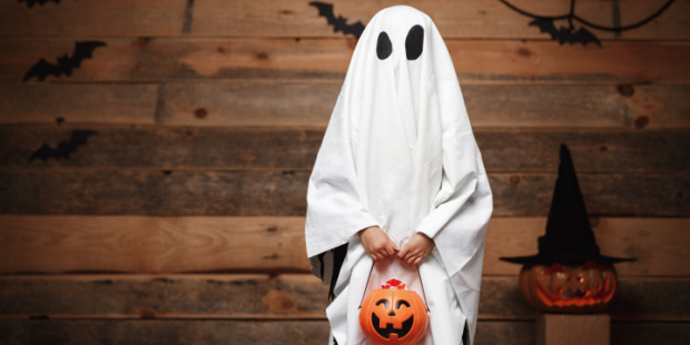 A person in a ghost costume holding a pumpkin.