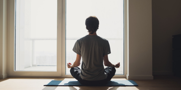 A man meditating in front of a large window. 