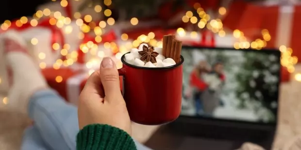 A woman relaxing in front of a movie, drinking hot chocolate, with Christmas decorations surrounding her. 