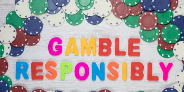 The words 'gamble responsibly' spelled out on a wooden table surrounded by poker chips. 