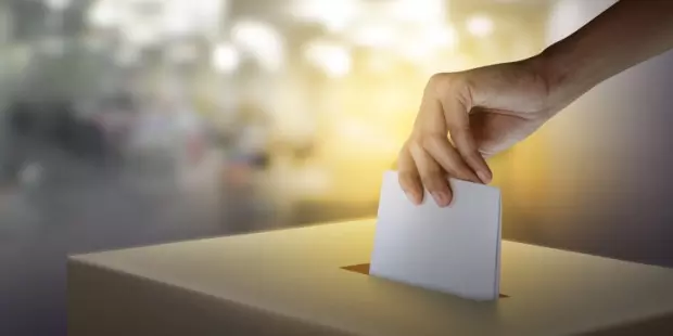 A woman's hand placing a ballot into the ballot box on election day. 