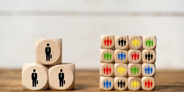 A stack of three wooden cubes with people drawn on them vs a large stack with drawings of dozens of people. 