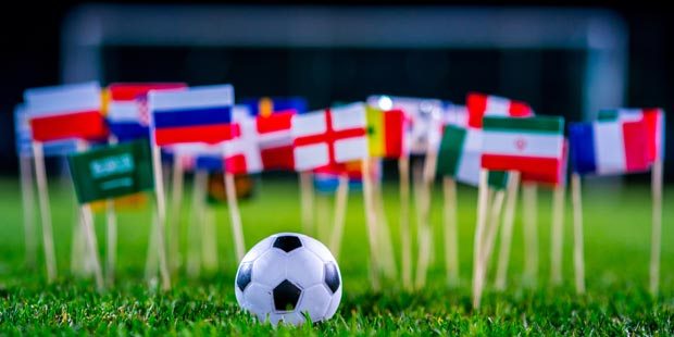 A soccer ball surrounded by international flags on green grass