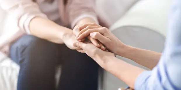 Two women holding hands in support of one another. 
