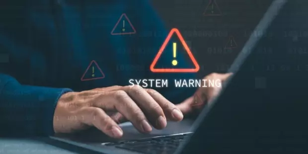 A system warning pops up while a man types on a laptop. 