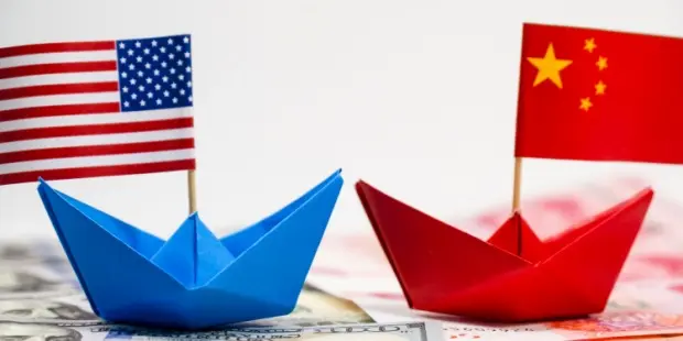 Two paper ships with the American and Chinese flags facing each other on a bed of banknotes. 