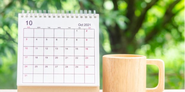 A calendar showing the month of October, near a wooden mug.