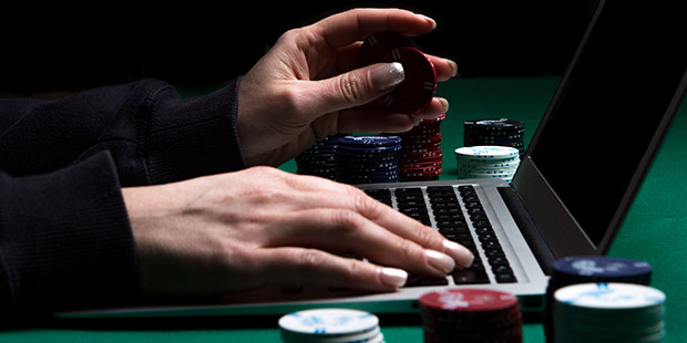 A laptop opened to Everygame Poker with chips around and a player's hands on the keyboard.