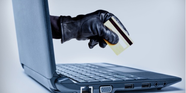 A gloved hand of a thief, holding a credit card, reaching out of a laptop screen. 
