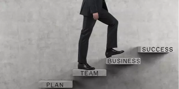 A businessman walking up stone steps, marking the path to success in business: idea, plan, team, business, success. 