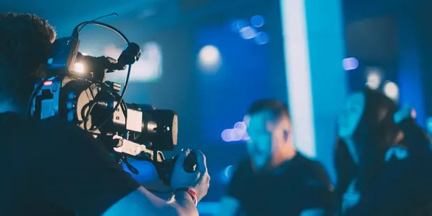 A cameraman taping an event, as two people sit in front of the camera. 