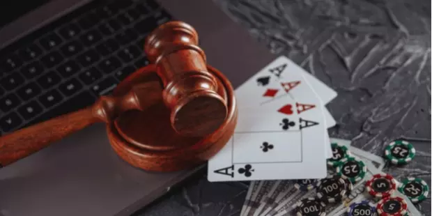 A judge's gavel laying on top of a laptop, appearing alongside cards, money, and poker chips. 