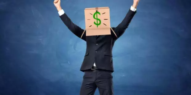 A man, hiding his face in a box with a dollar sign drawn on it, raises his hands in triumph. 