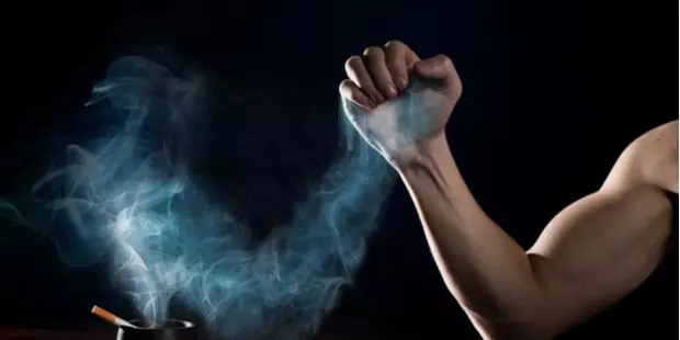 A man's hand arm-wrestling with a hand made of cigarette smoke. 