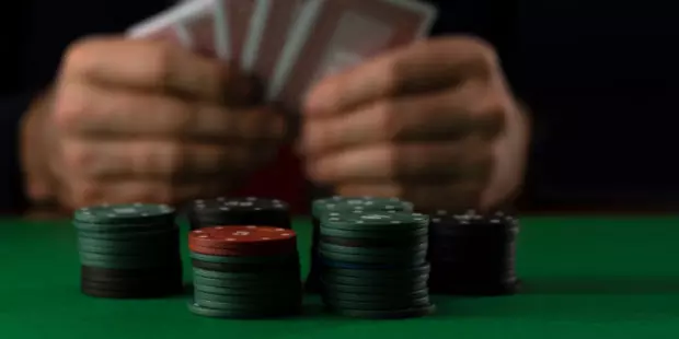 A stack of poker chips with a man holding playing cards in the background. 
