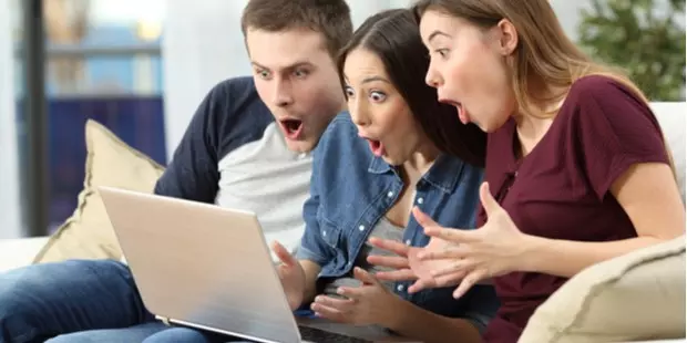 Three friends sitting on a couch and reading the news with a shocked expression