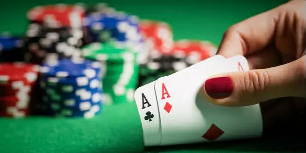 a woman's hand with red nail polish showing 2 aces with a poker table and casino chips in the background