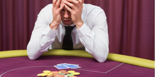 Man holding his head while sitting at the poker table.