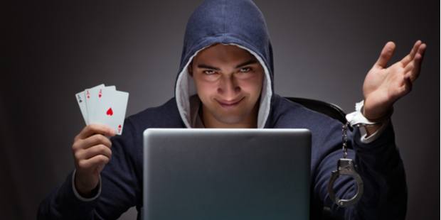 A man wearing a hoodie sitting in front of a laptop holding cards with handcuffs on