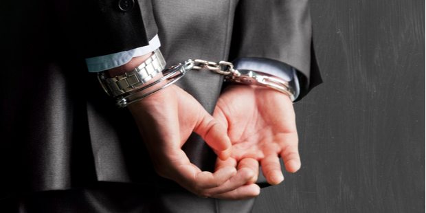 man in a suit with his hands in handcuffs behind his back.