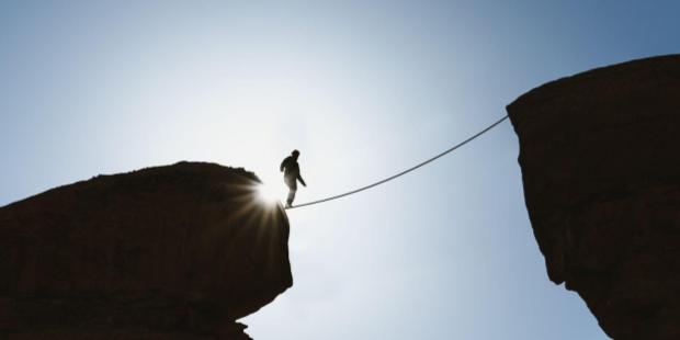 man waking on a tightrope stretched between two hills