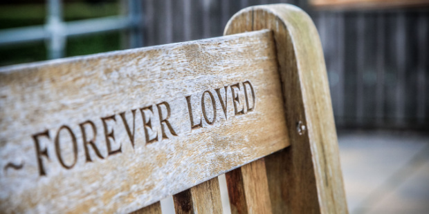 The words "forever loved" engraved on a wooden bench.
