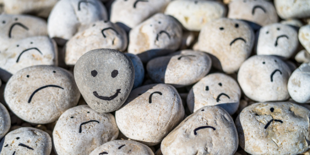 Happy and sad smiley faces drawn on stones.