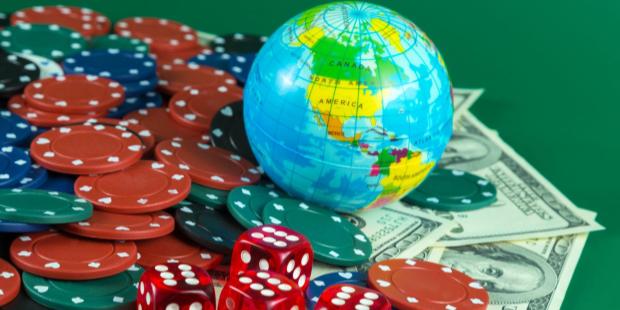 An earth globe, poker chips, and dice lying on a stack of cash.  