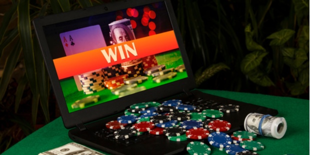 A pile of poker chips and a stack of cash lying on a laptop, while the screen shows the word "win". 
