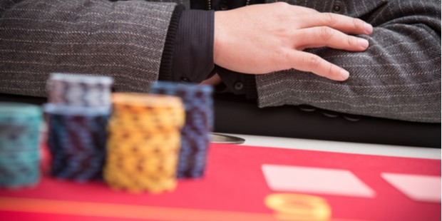 A photo of a player sitting at a table with folded hands, a pile of poker chips nearby.