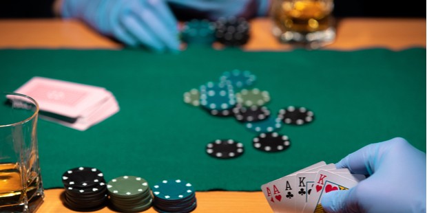 Poker chips next to a whisky glass, with poker cards in a gloved hand.
