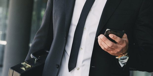 a man in a suit holding a briefcase in one hand, and his mobile phone in the other hand