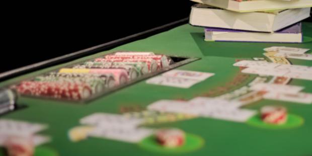 A stack of books placed on a poker table, with cards and poker chips lying around. 