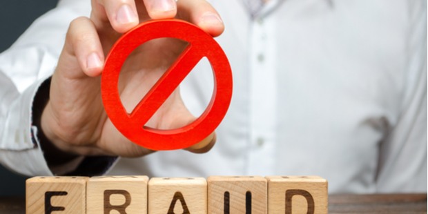 A man holding a red warning sign over wooden blocks that spell the word FRAUD.