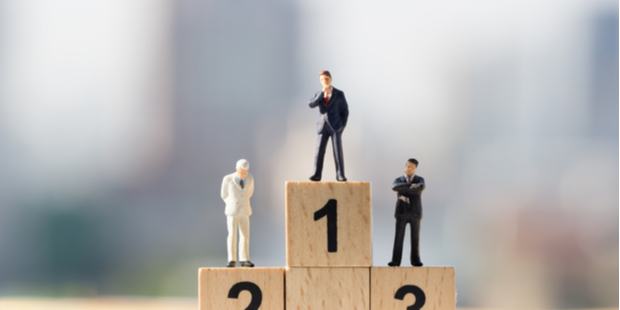 Three miniature people standing on a podium made of wooden blocks.