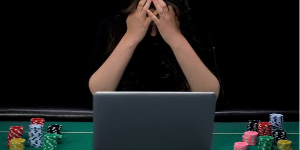 A woman sadly sitting in front of a laptop placed on a poker table. 