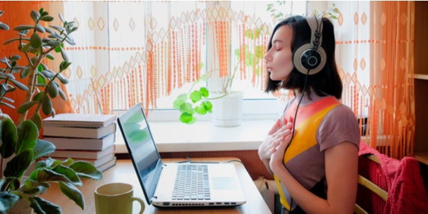 A woman breathing deeply and listening to music while sitting in front of a computer. 
