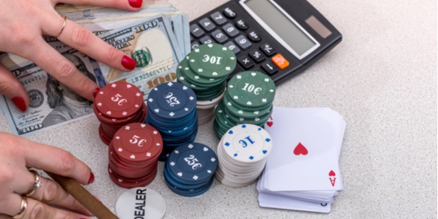 Woman's hands holding on to a stack of cards, cash, poker chips, and a calculator.