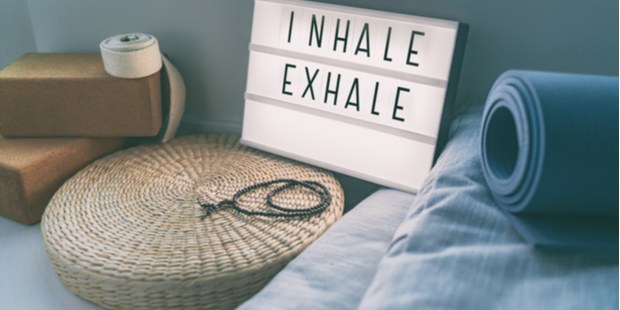 words Inhale and Exhale, written on a sign next to a yoga mat and a meditation pillow.