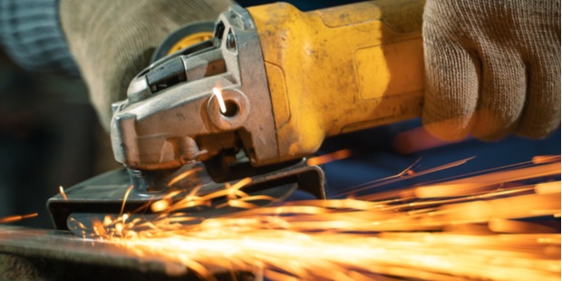 A worker using a grinder to process metal, with sparks flying around. 
